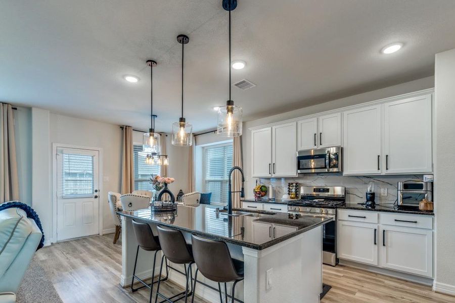 This modern kitchen features sleek white cabinetry, stainless steel appliances, and a spacious island with bar seating. Pendant lighting adds elegance, while large windows provide ample natural light. The open layout connects seamlessly to the living area, perfect for entertaining.
