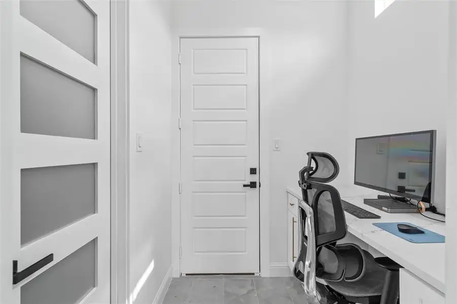 Dedicated workspace featuring a built-in desk with a light-toned countertop, custom cabinetry, and a modern five-panel door with matte black hardware