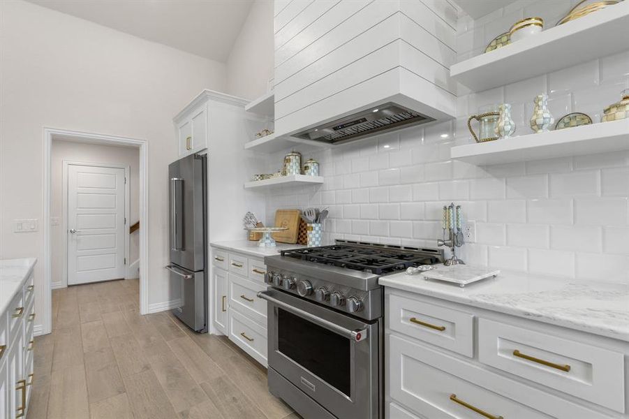 Kitchen with open shelves, high end appliances, white cabinetry, decorative backsplash, and premium range hood Kitchen with open shelves, high end appliances, white cabinetry, decorative backsplash, and premium range hood
