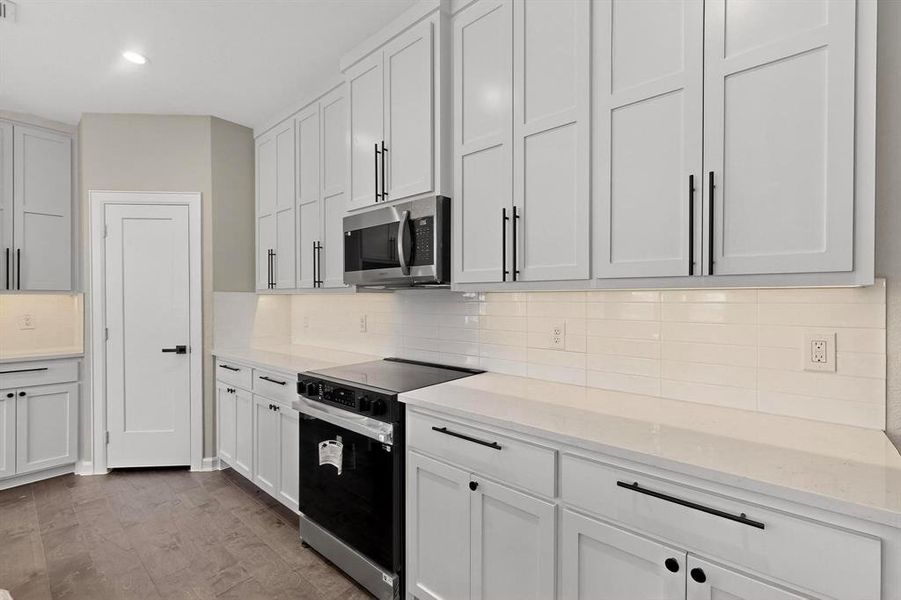 Kitchen with electric stove, stainless steel microwave, backsplash, light stone counters, and recessed lighting Kitchen with electric stove, stainless steel microwave, backsplash, light stone counters, and recessed lighting