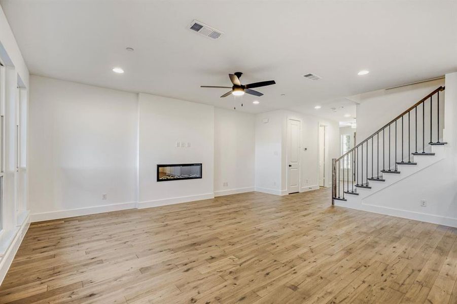Unfurnished living room featuring light wood-type flooring, a ceiling fan, a glass covered fireplace, and recessed lighting