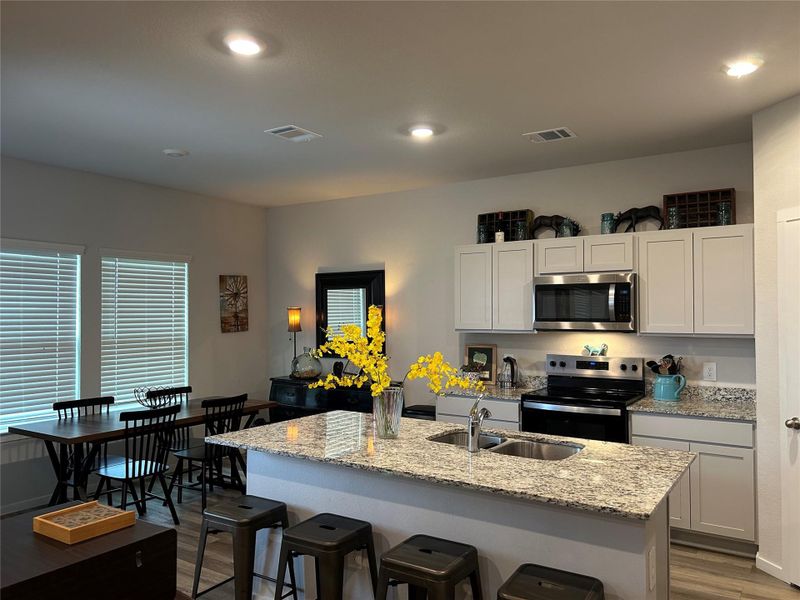 Open-concept kitchen and dining area featuring a granite-topped island with an undermount sink, stainless steel appliances, light cabinetry, and wood-finish flooring