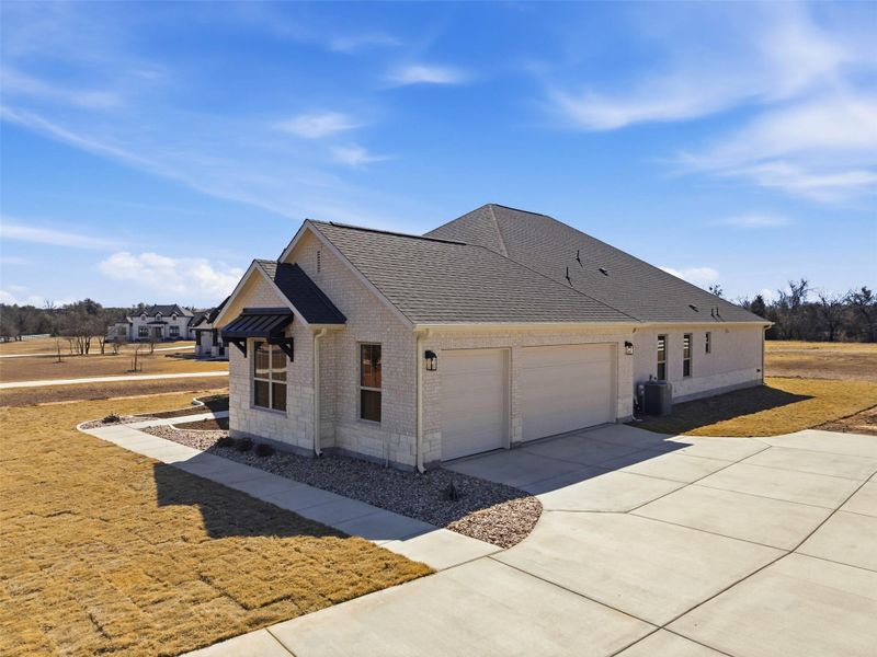 View of side of home featuring brick siding, roof with shingles, driveway, and an attached garage
