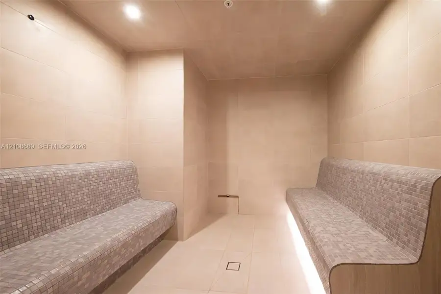 Steam room featuring large-format wall and floor tiling, dual built-in benches with mosaic tile surfacing, and recessed toe-kick lighting