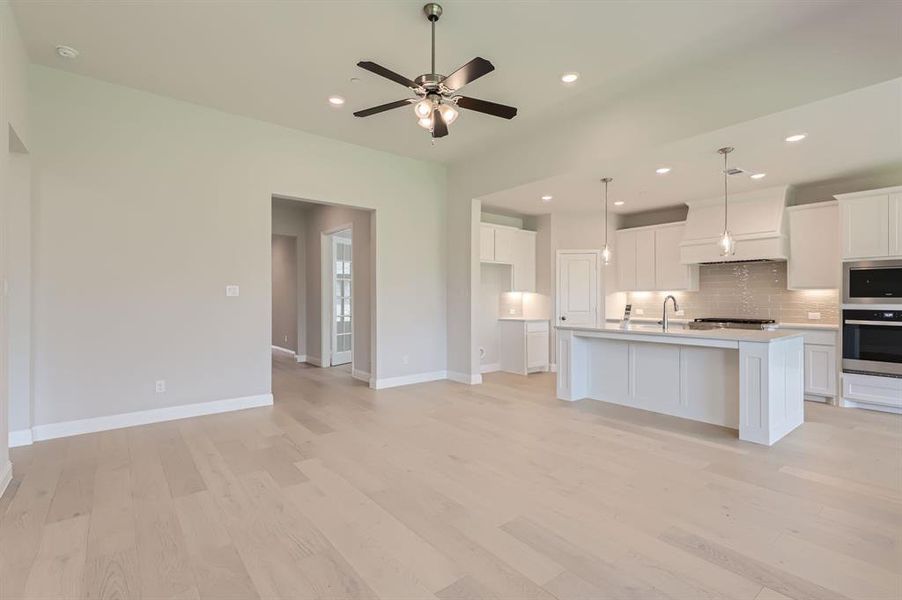 Kitchen featuring appliances with stainless steel finishes, a center island with sink, backsplash, decorative light fixtures, and ceiling fan