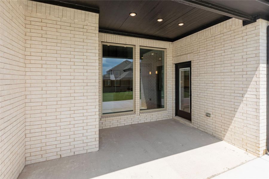 Covered back patio with white brick walls, dark wood ceiling, recessed lights, and glass door entry.