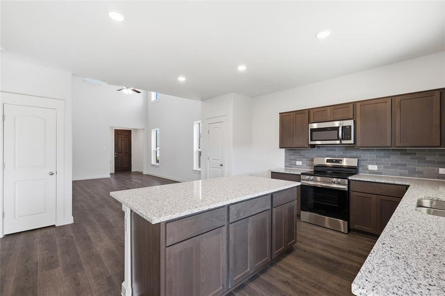 Kitchen featuring a central island with a light-toned countertop, wood-finish flooring, dark wood cabinetry, and stainless steel appliances