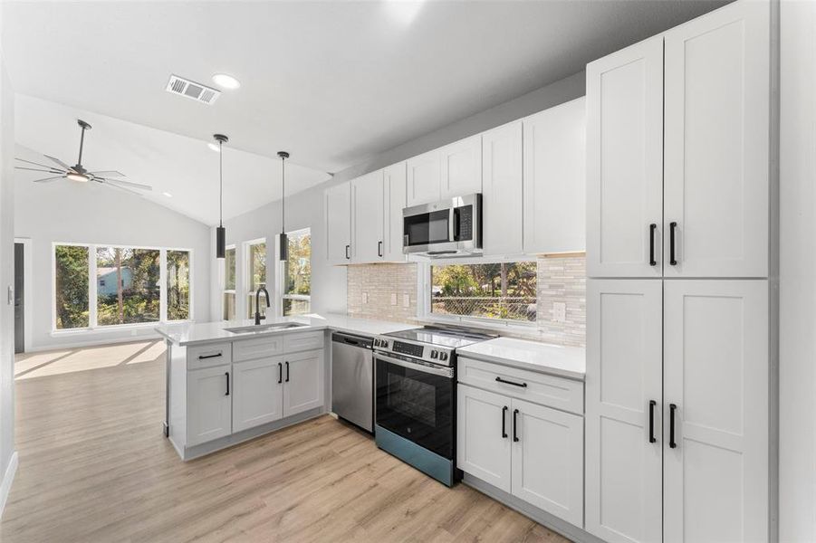 Kitchen with appliances with stainless steel finishes, white cabinetry, recessed lighting, lofted ceiling, and a peninsula