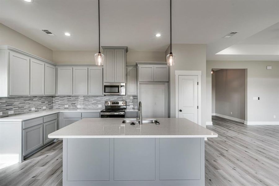 Kitchen with backsplash, light hardwood / wood-style floors, appliances with stainless steel finishes, and sink