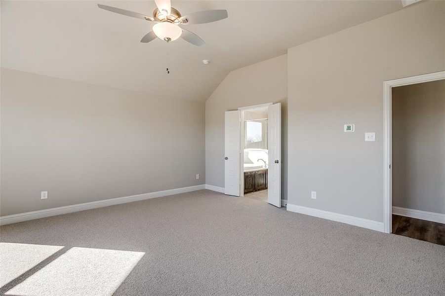 Unfurnished bedroom with vaulted ceiling, ensuite bath, ceiling fan, and light carpet Unfurnished bedroom with vaulted ceiling, ensuite bath, ceiling fan, and light carpet