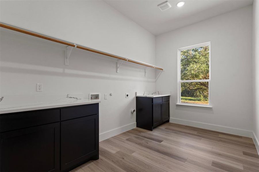 Laundry area with gas dryer hookup, washer hookup, light wood finished floors, hookup for an electric dryer, and cabinet space