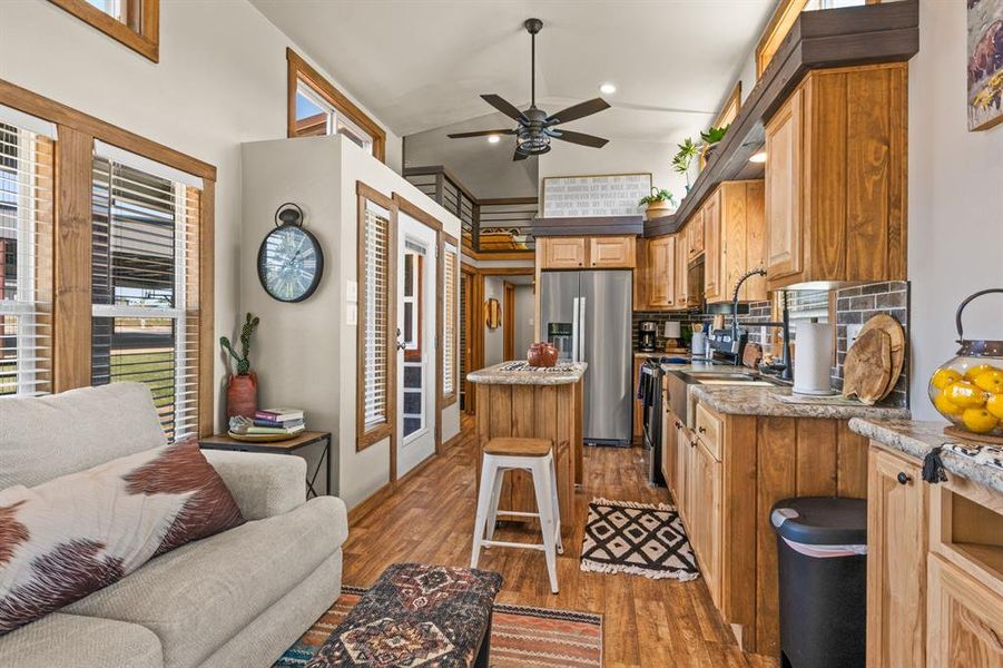 Kitchen with light wood-style flooring, stainless steel refrigerator with ice dispenser, decorative backsplash, brown cabinets, and a ceiling fan
