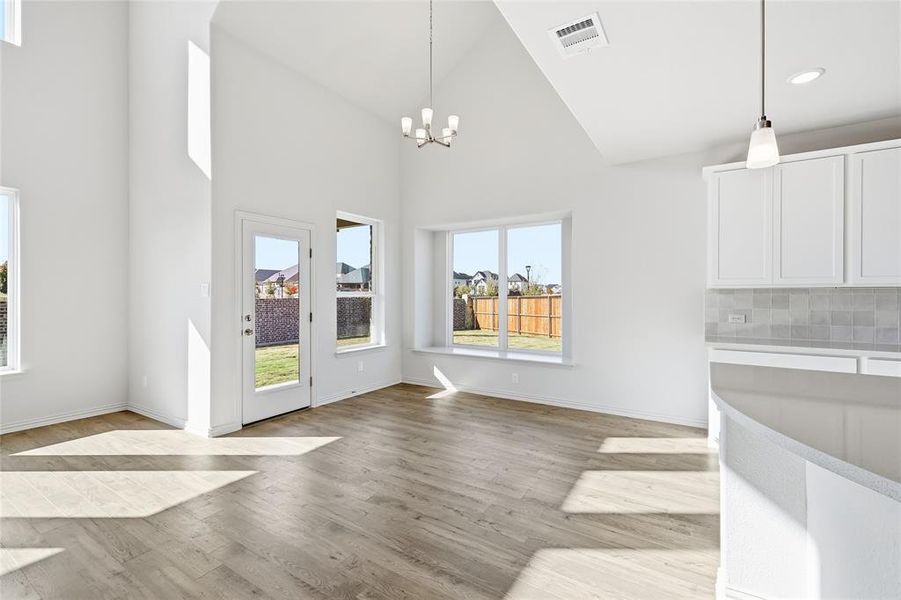 Unfurnished dining area featuring light wood-type flooring, a chandelier, and high vaulted ceiling