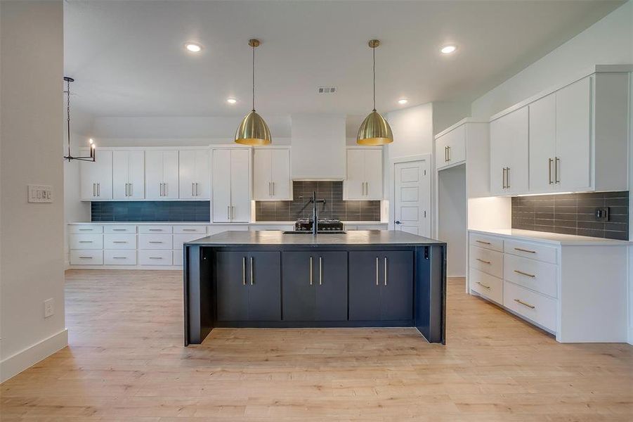 Kitchen featuring hanging light fixtures, a center island with sink, white cabinets, and tasteful backsplash