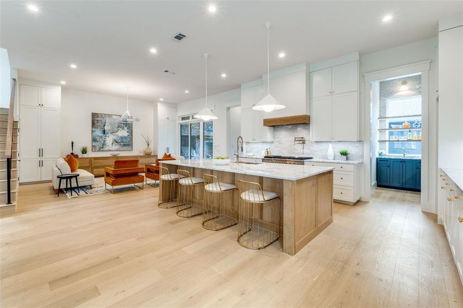 Kitchen featuring sink, white cabinets, a large island with sink, hanging light fixtures, and light stone countertops