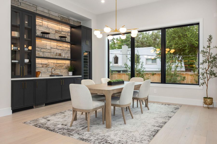 This elegant dining area blends simplicity with thoughtful design, featuring soft textures and a cohesive palette. Large windows create a connection to the outdoors while filling the room with light. The standout feature is the statement chandelier, adding a sculptural element that elevates the entire space and creates a warm, inviting atmosphere.