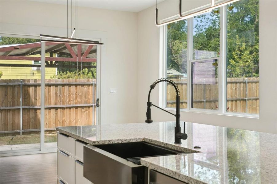 Kitchen featuring hanging light fixtures, a healthy amount of sunlight, hardwood / wood-style floors, and light stone countertops