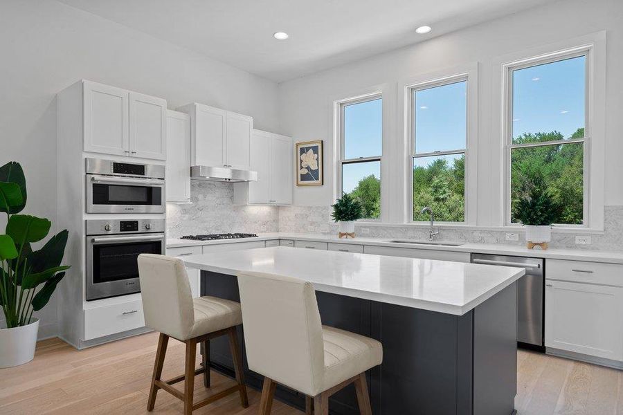 Chef-inspired kitchen showcasing a waterfall-edge island with room for eat-in seating, custom cabinetry, high end Bosch stainless steel appliances, and abundant natural light.