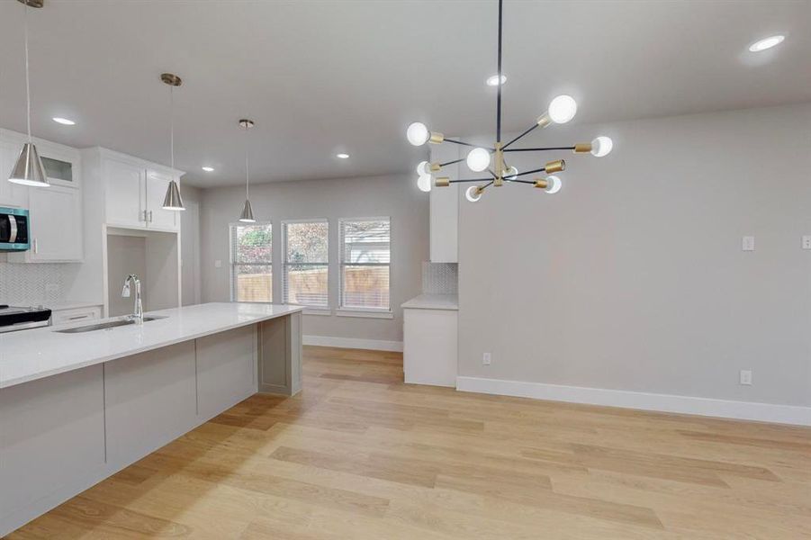 Kitchen featuring white cabinetry, sink, hanging light fixtures, backsplash, and light wood-type flooring