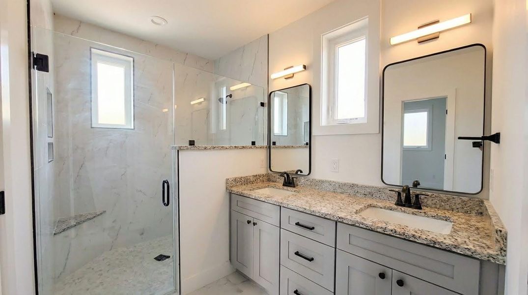 Bathroom with a marble finish shower, double vanity, and light marble finish flooring