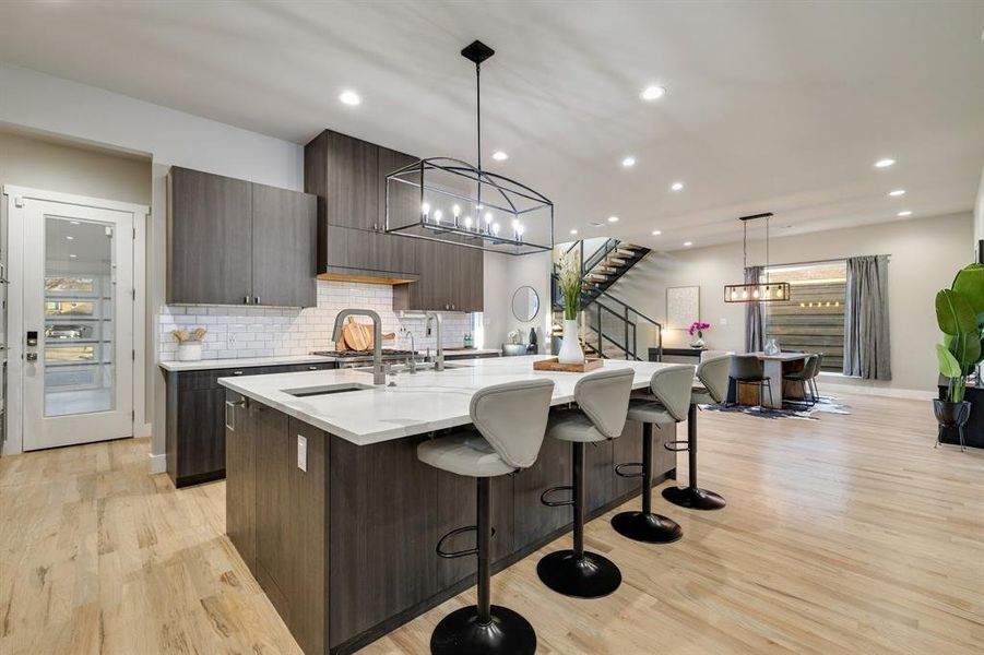 Kitchen featuring hanging light fixtures, an island with sink, light wood-type flooring, a kitchen bar, and dark brown cabinets