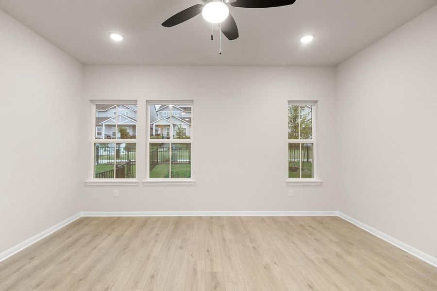 This room features light-colored walls, light wood-style flooring, and three windows providing views of the surrounding neighborhood