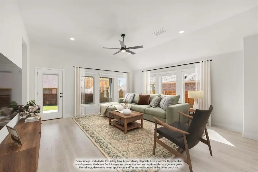 Living room with vaulted ceiling, ceiling fan, green sectional sofa, and light hardwood floors with large windows.