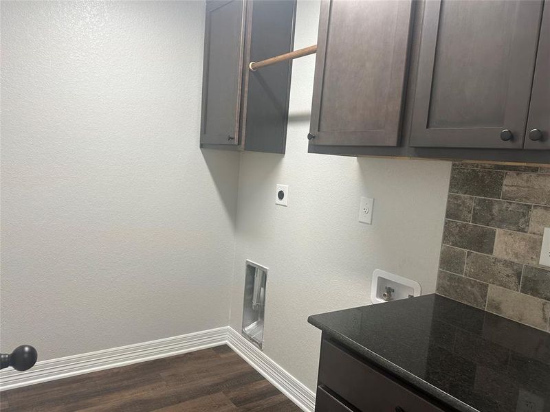 Washroom with electric dryer hookup, hookup for a washing machine, cabinet space, and dark wood-style flooring