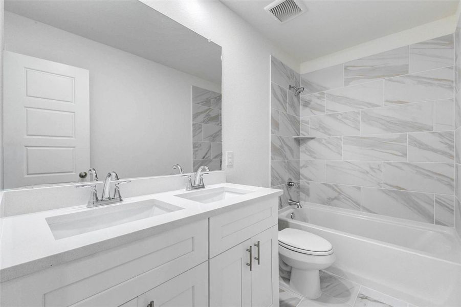 Secondary bathroom featuring a bright double-sink vanity, white cabinetry, chrome fixtures, large mirror, and a tub/shower combo with marble-look tile surround. The clean neutral finishes create a polished, modern look while offering everyday functionality for guests or secondary bedrooms.
