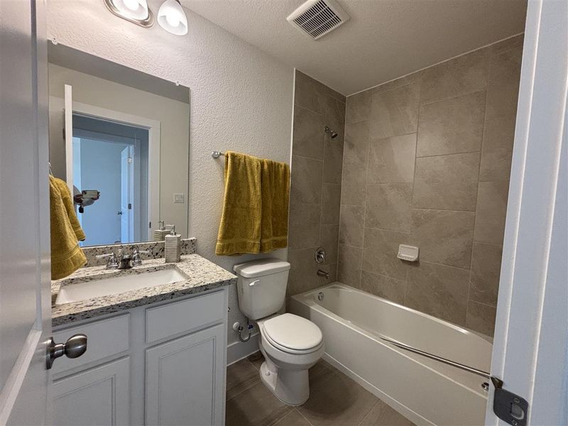 Full bathroom featuring toilet, a textured ceiling, tiled shower / bath, and vanity