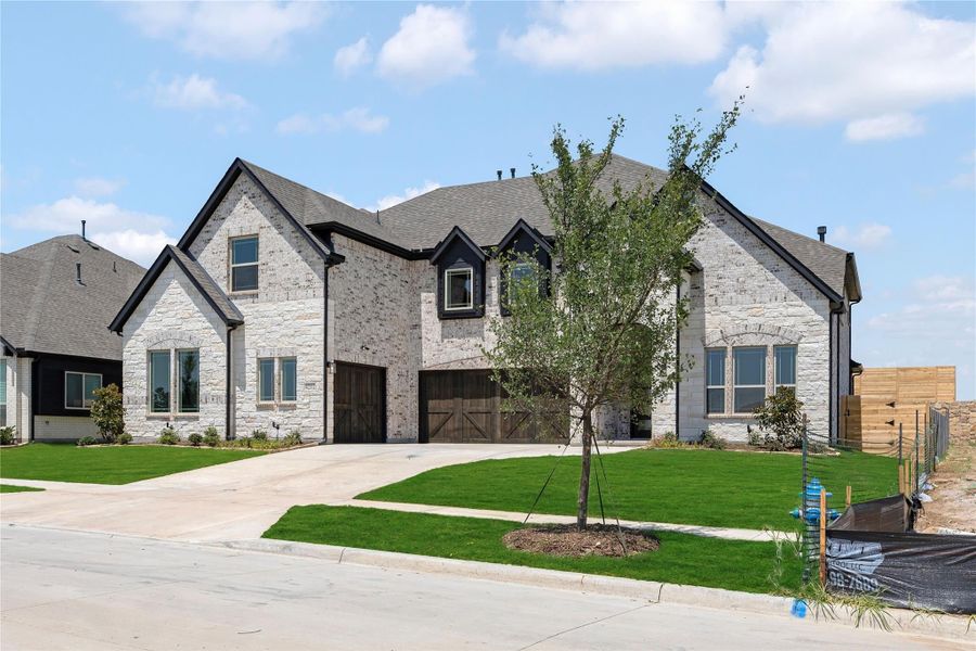 Two-story stone home with dark wood garage doors, gray roof, and green front lawn