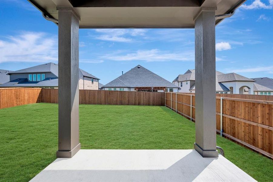 Covered patio featuring a concrete slab and painted support columns overlooking a fenced backyard with a manicured lawn