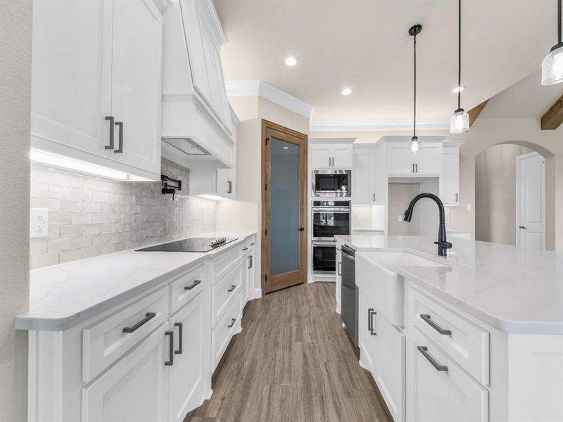 Kitchen with pendant lighting, hardwood / wood-style floors, white cabinets, an island with sink, and appliances with stainless steel finishes