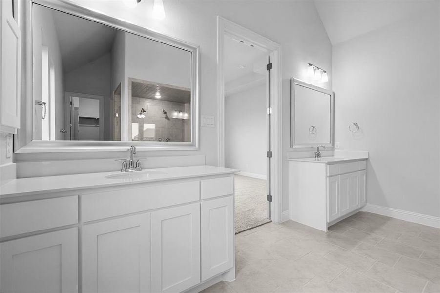 Full bath with tiled shower, two vanities, lofted ceiling, and baseboards Full bath with tiled shower, two vanities, lofted ceiling, and baseboards
