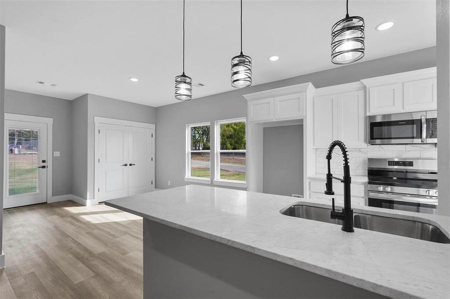 Kitchen with white cabinets, tasteful backsplash, decorative light fixtures, appliances with stainless steel finishes, and light stone countertops