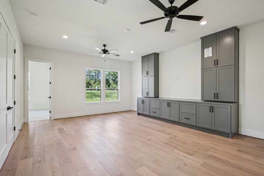 Spacious, bright room with hardwood floors, two ceiling fans, large windows, and built-in gray cabinetry. Ideal for a versatile living area.