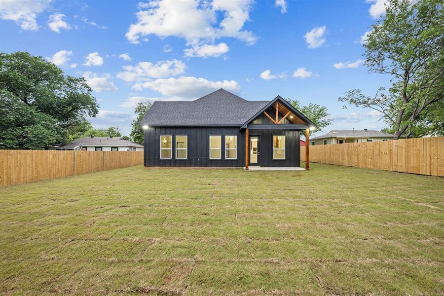Expansive fenced backyard featuring new turf, a covered patio with exposed wood beams, and a dark-paneled exterior Expansive fenced backyard featuring new turf, a covered patio with exposed wood beams, and a dark-paneled exterior