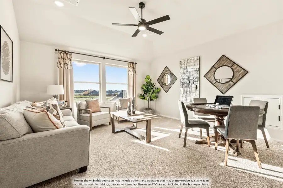 Open-plan living and dining area with carpet, ceiling fan, large windows, and round dining table with gray chairs.