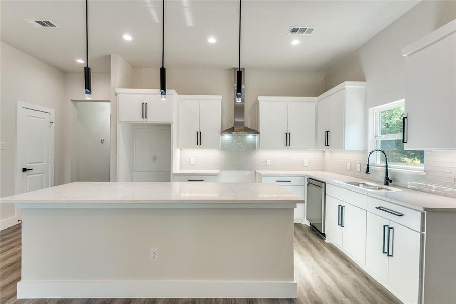 Kitchen with wall chimney range hood, sink, a kitchen island, and light hardwood / wood-style flooring