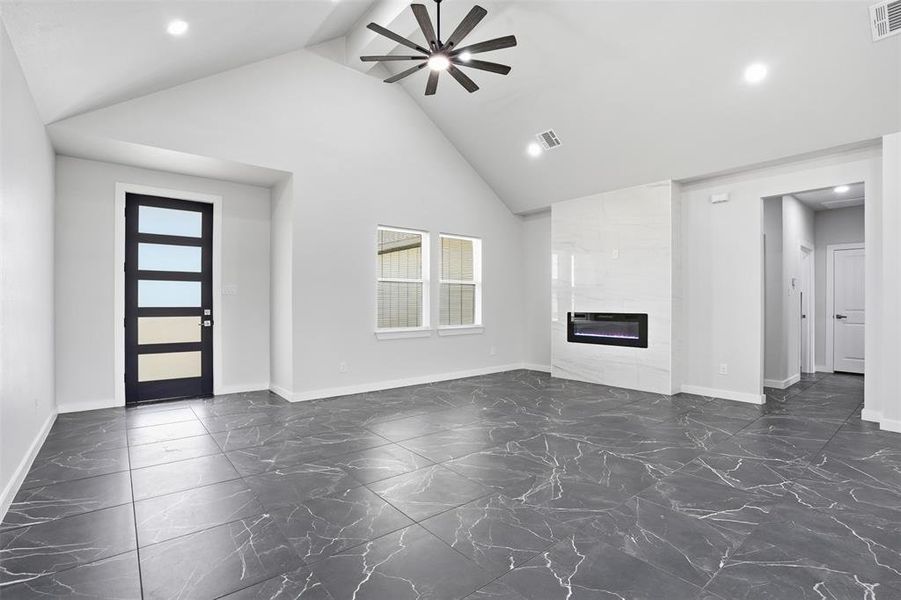 Spacious room featuring vaulted ceilings, recessed lighting, and large format dark tile flooring with light veining