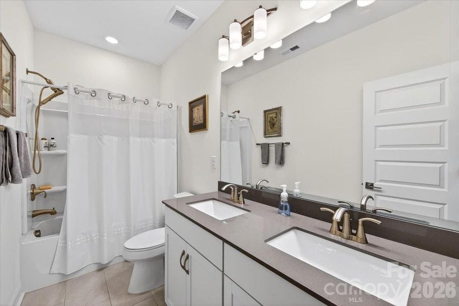 Guest bathroom with quartz countertop dual vanity and tiled floors.