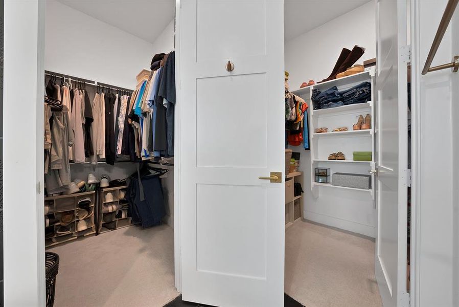 Walk-in closet featuring white panel doors with brass hardware, built-in shelving, hanging rods, and light-toned carpeting Walk-in closet featuring white panel doors with brass hardware, built-in shelving, hanging rods, and light-toned carpeting