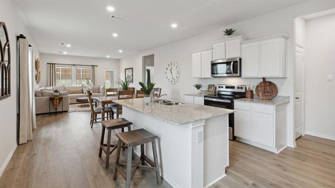 Kitchen with stainless steel appliances, white cabinets, light stone counters, a kitchen breakfast bar, and recessed lighting