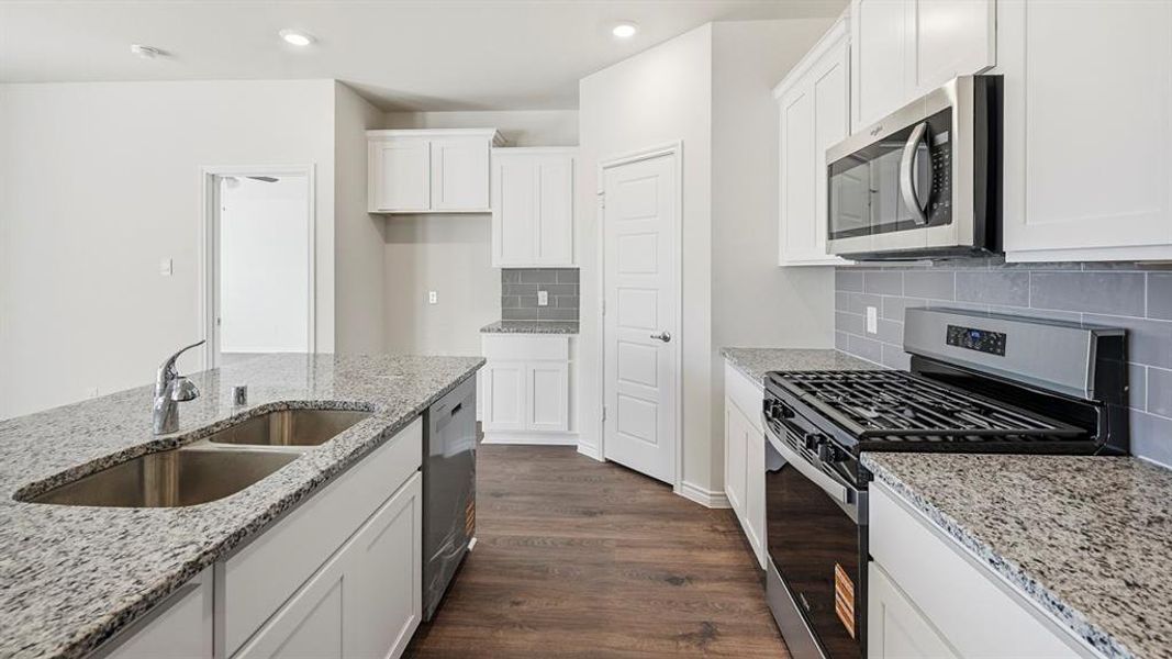 Kitchen with stainless steel appliances, dark wood-type flooring, white cabinets, decorative backsplash, and light stone counters Kitchen with stainless steel appliances, dark wood-type flooring, white cabinets, decorative backsplash, and light stone counters