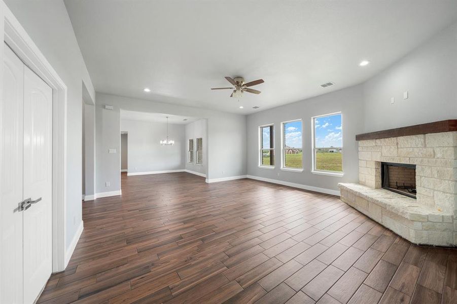 Unfurnished living room with ceiling fan with notable chandelier, a stone fireplace, and dark wood-type flooring