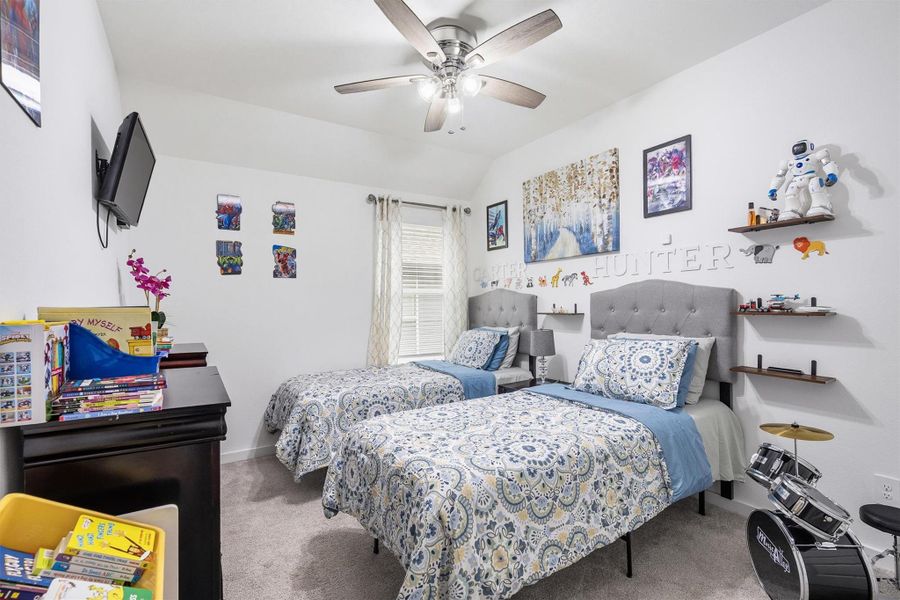 This bedroom offers a window with privacy blinds, soft carpeting, and a ceiling fan, providing a bright and comfortable space perfect for rest and relaxation.
