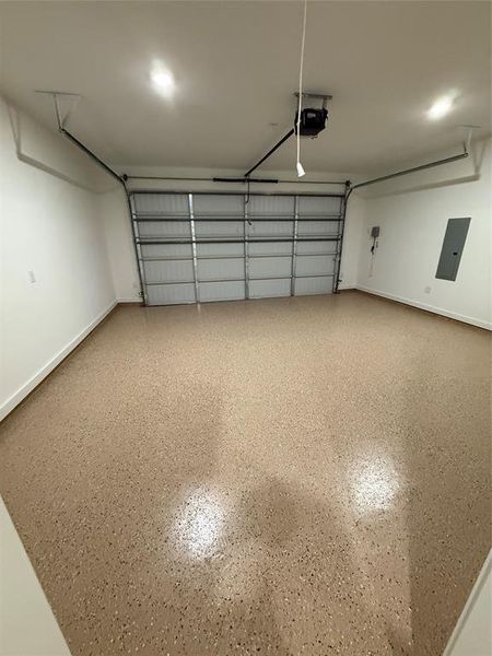 Garage with electric panel, a garage door opener, and baseboards