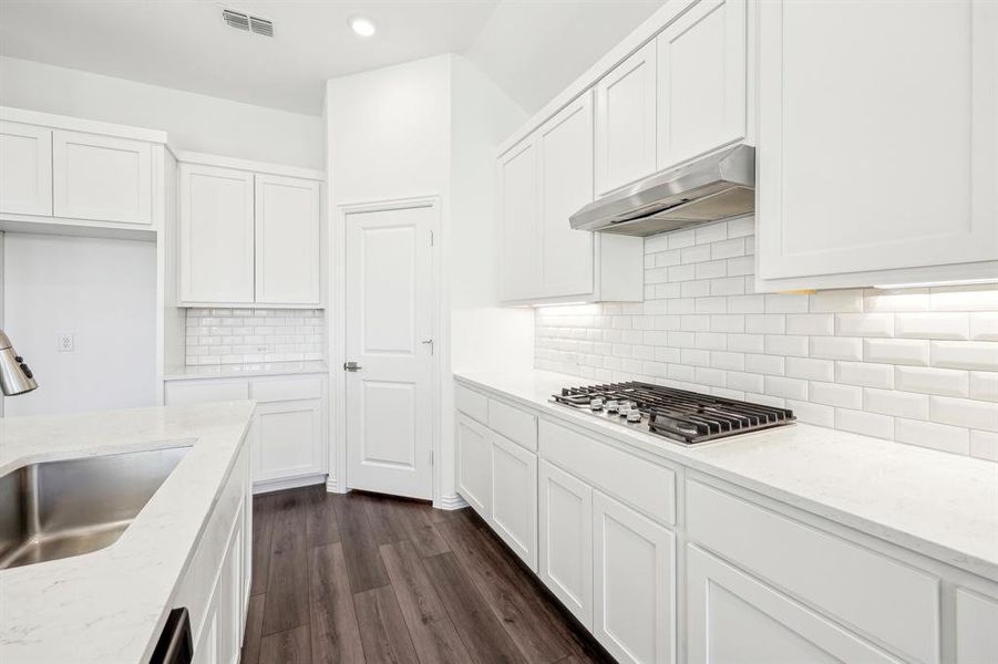 Kitchen with stainless steel gas stovetop, white cabinets, light stone counters, and sink