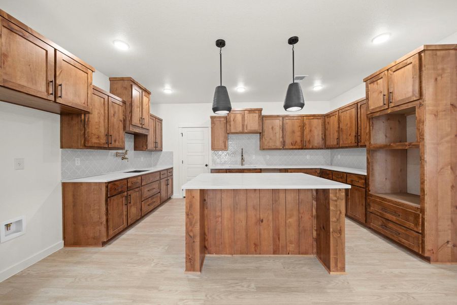A well-lit culinary space features abundant wood cabinetry and a central island with sleek pendant lighting.