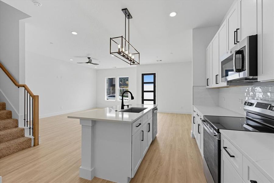 Kitchen featuring appliances with stainless steel finishes, decorative light fixtures, white cabinets, light wood-style floors, and a chandelier